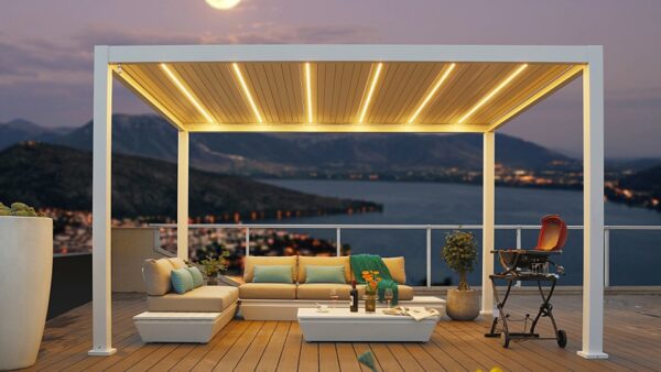 Nowoczesne patio na dachu o zmierzchu oferuje Oświetlenie LED do pergoli lamelowej na wymiar z ciepłym światłem, przytulną sofę segmentową z kolorowymi poduszkami, stół z napojami, rośliny doniczkowe i wysokie krzesło z widokiem na malownicze jezioro i góry.