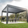 Nowoczesna pergola z dachem z listew stoi na patio, osłaniając stół i cztery krzesła - to eleganckie zadaszenie tarasu otoczone jest zielonym trawnikiem i drzewami pod częściowo zachmurzonym niebem.