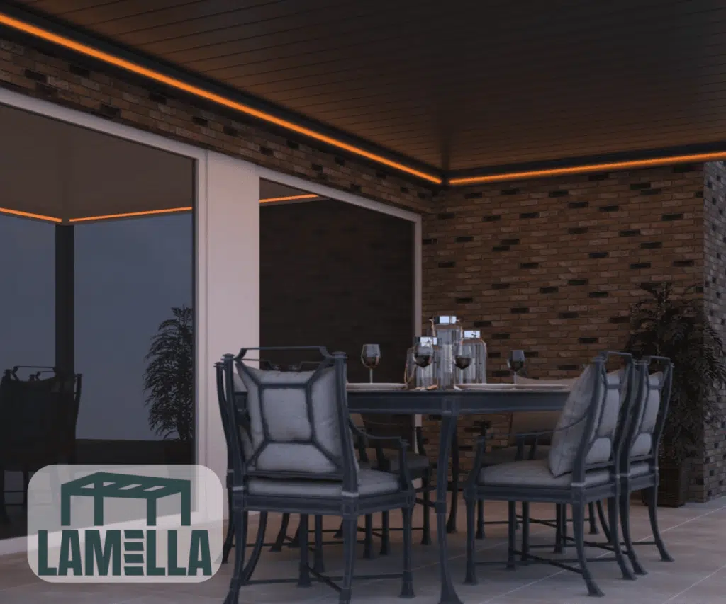 Patio na świeżym powietrzu z Lamellendach manuell (kopia), czarnym stołem jadalnym z sześcioma wyściełanymi krzesłami, zestawem szklanek i talerzy. Ciepłe oświetlenie taśmowe LED podkreśla sufit pergoli. Logo Lamella w lewym dolnym rogu.