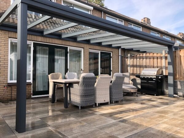 Nowoczesne patio z Zadaszeniem tarasowym ze szkła, stołem dla sześciu osób i grillem gazowym na kamiennych płytkach obok ceglanego domu z przesuwanymi szklanymi drzwiami i eleganckim dachem lamelowym elektrycznym.