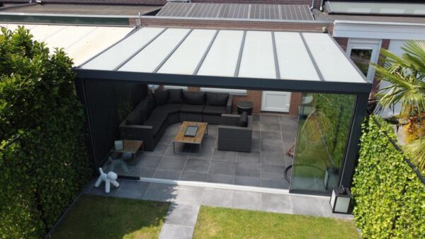 Nowoczesne patio na świeżym powietrzu z Zadaszeniem tarasowym ze szkła, szklanymi ścianami, narożną sofą, stolikiem kawowym, dekoracyjną rzeźbą białego niedźwiedzia, bujną zielenią i palmą pod elegancką pergolą.